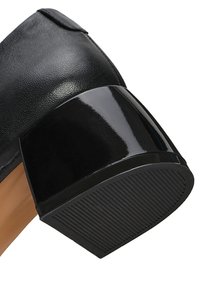 Scarpa in pelle nera con tacco a blocco nero lucido. La suola presenta un motivo testurizzato a righe per una migliore aderenza. Finitura liscia complessiva.