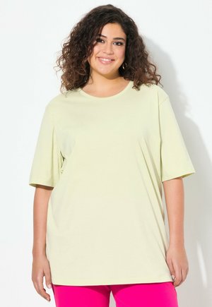 T-shirt oversized di un giallo chiaro con maniche corte e scollatura rotonda. Tessuto morbido, stoffa liscia, abbinata a pantaloni rosa acceso.