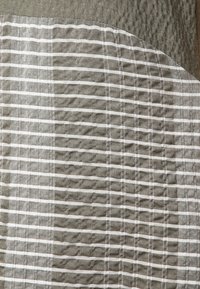 Gros plan d'un tissu texturé avec des rayures blanches horizontales et verticales sur un fond marron clair, plié à l'angle.