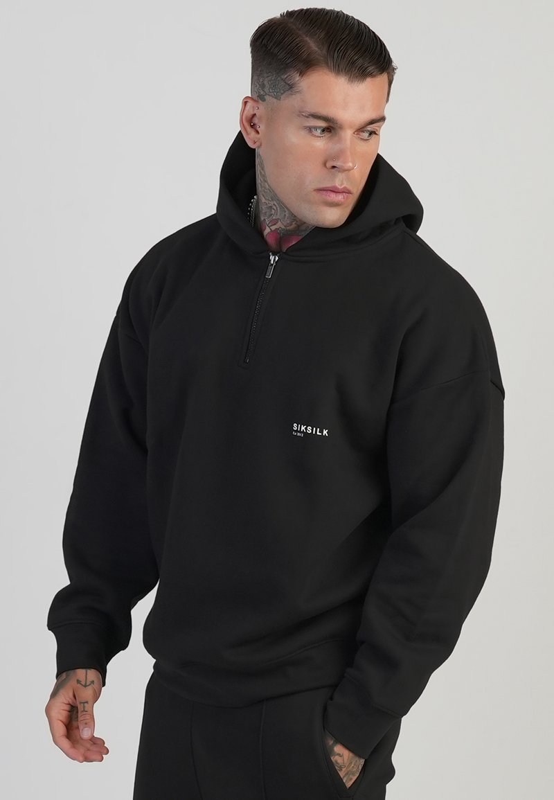 Zwarte zip-up hoodie gemaakt van een zachte stof, met een kangoeroezak en een klein logo op de borst. Soepele textuur en een ontspannen pasvorm.