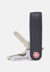 Porte-clés en cuir noir, comportant un multi-outil en métal argenté avec des fentes pour clés, une texture embossée et un accent croix suisse rouge.