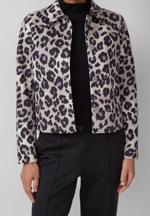 Mujer con chaqueta corta de estampado de leopardo con botones sobre un jersey negro acanalado de cuello vuelto y pantalones negros de tiro alto.
