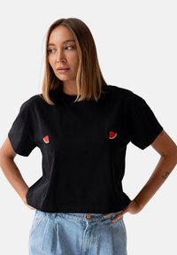Czarna, krótka koszulka z bawełny, z dwoma aplikacjami w kształcie plasterków arbuza na piersi. Krótkie rękawy i luźny krój.