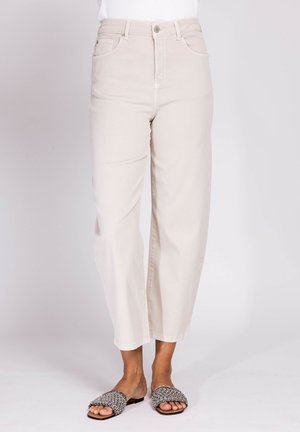 Beige hoch taillierte Hose mit geradem Bein, kombiniert mit weißem Top und schwarz-weißen, gewebten Slip-On-Sandalen vor neutralem Hintergrund.