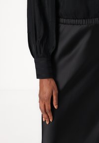 Black blouse with long, puffed sleeves and striped cuffs, paired with a smooth black skirt. Material appears soft and silky.