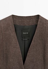 Bruine getextureerde blazer met een diepe V-hals en een zwarte voering waarin een 'Massimo Dutti' label is gestikt.