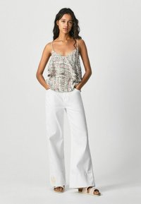 Top floral de capas con tirantes finos; combinado con pantalones blancos de pierna ancha. Los tirantes y el dobladillo tienen detalles que crean un aspecto texturizado.