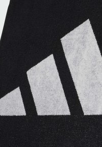 Crni tekstil s velikim bijelim trokutastim logotipom. Površina ima teksturirani izgled s suptilnim sjajem.