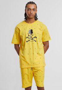 Żółty zestaw t-shirt i szorty z bawełny, z nadrukiem czarnych czaszek i skrzyżowanych kości, z małymi motywami czaszek rozproszonymi na całej powierzchni.