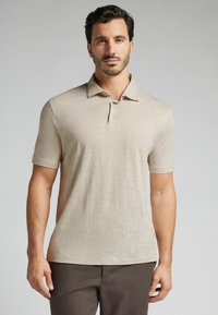 Béžové polo triko s krátkým rukávem a límečkem, se třemi knoflíky, vyrobené z lehkého materiálu, s hladkým povrchem.