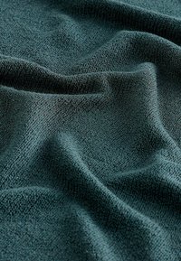 Teksturoitu, tummanvihreä kangas, jossa on pehmeä, kudottu ilme ja joka osoittaa hienovaraisia vaihteluita tekstuurissa ja syvyydessä laskoksissa.