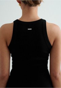 Must mustriga tank top musta värviga, millel on ümar kaelus ja väike hõbedane ristkülikukujuline logo tagaküljel. Tihedalt ligipääsetav disain rõhutab kuju.
