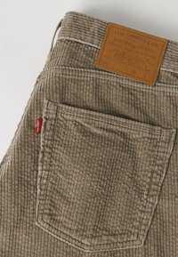 Бежови панталони от кадифе Levi's с видими шевове, червен етикет Levi's и кафява кожена етикета на талията.