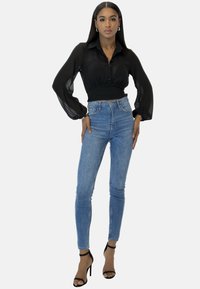 Blusa nera trasparente a maniche lunghe con bottoni, jeans skinny blu chiaro a vita alta e décolleté neri con tacco a spillo. Silhouette sagomata e aderente.