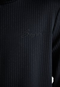 Tissu de costume bleu marine foncé avec des rayures verticales. Comprend un logo "Boss" brodé dans un design ton sur ton discret.