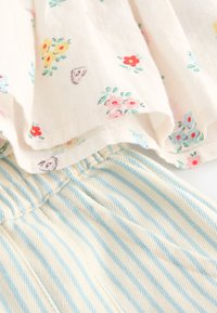 Tissu léger avec imprimé floral coloré associé à un tissu texturé rayé verticalement crème et bleu clair.