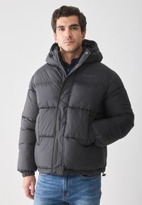 Chaqueta de plumas negra con capucha, que presenta un diseño acolchado y puños elásticos. Adecuada para el clima frío con un ajuste informal.