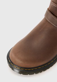 Brown leather boot with a rounded toe, featuring a black rubber sole and yellow stitching along the edge. Smooth texture and minimal design.