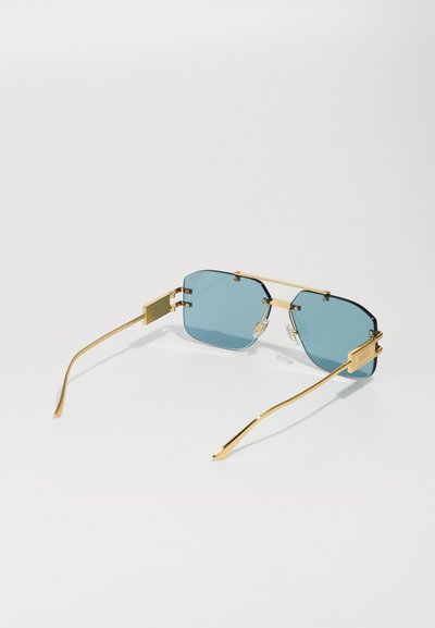 Occhiali da sole in metallo dorato con lenti blu, forma ottagonale e dettagli decorativi sul telaio.