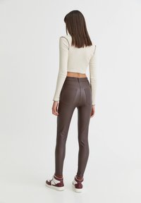 Leggings en similicuir marron à taille haute, avec deux poches arrière et une coupe ajustée, assortis à des baskets blanches et bordeaux.