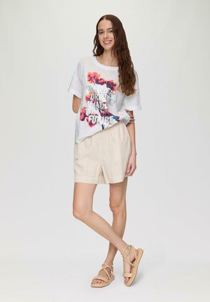 White t-shirt with colorful floral graphic and text, paired with light beige, pinstriped shorts and tan strappy sandals. Minimalist design.