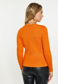 Pulover tricotat portocaliu cu un design ajustat și mâneci lungi. Textură netedă, guler rotund. Asortat cu pantaloni negri ajustați.