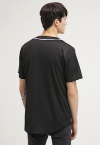 T-shirt noir à manches courtes en tissu lisse, avec un ourlet arrondi et un accent blanc au niveau du col, vu de dos.