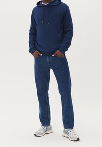 Felpa blu navy con cordoncini, abbinata a jeans di denim blu e sneakers argentate con dettagli blu. Texture liscia, vestibilità casual, design minimale.