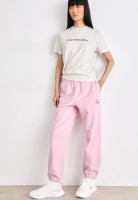 Lichtgrijze t-shirt met het logo "Calvin Klein Jeans", gecombineerd met roze joggingbroeken met een geborduurd logo, en witte sneakers.