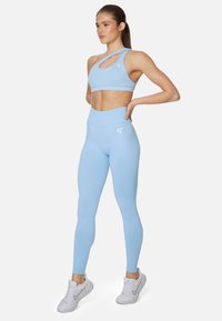 Light blue sports bra with a unique asymmetric cut and cut-out feature, paired with matching high-waisted leggings, both made of smooth fabric.