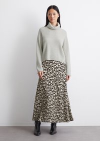 Lys grå ribbestrikket turtleneck genser kombinert med en flytende beige skjørt med et svart abstrakt mønster, supplert med svarte ankelstøvler.