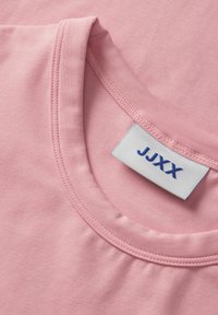 Close-up van een roze T-shirt halslijn met een wit label waarop "JJXX" in blauwe tekst staat.