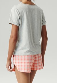 Szary t-shirt z krótkim rękawem i mankietami, połączony z różowo-białymi szortami w kratę z bocznymi rozcięciami, wykonanymi z miękkiego materiału.