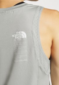 Osoba v šedém bezrukávovém topu s logem The North Face a názvy hor včetně jejich výšek a let prvního ženského výstupu na zádech.