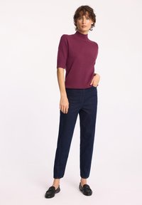 Dopasowany sweter z krótkim rękawem i wysokim kołnierzem w głębokim burgundzie. W połączeniu z ciemnoniebieskimi dżinsami o prostym kroju i czarnymi mokasynami. Gładka tekstura.