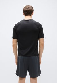 Μαύρο αθλητικό μπλουζάκι με κοντά μανίκια και λεία υφή, σε συνδυασμό με σκούρο γκρι σορτς που διαθέτουν πλέγμα για καλύτερο αερισμό.