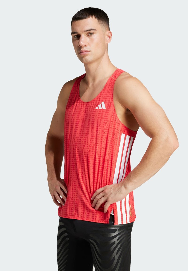 Red athletic tank top featuring a textured pattern, white Adidas logo, and three white stripes on each side. Worn with black patterned leggings.