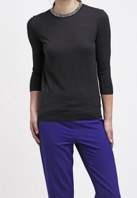 Zwarte gebreide trui met een kraagdetail van kralen, driekwartmouwen, gecombineerd met paarse broek. Soepele textuur, nauwsluitend ontwerp.