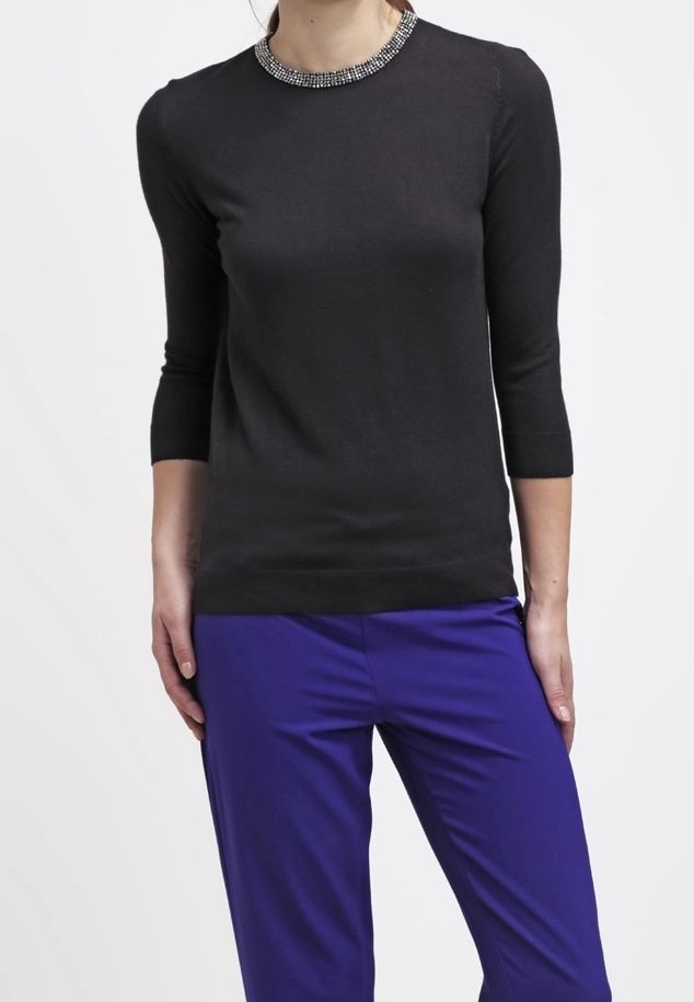 Zwarte gebreide trui met een kraagdetail van kralen, driekwartmouwen, gecombineerd met paarse broek. Soepele textuur, nauwsluitend ontwerp.