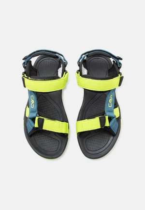 Μαύρα και νέον κίτρινα υπαίθρια σανδάλια με ρυθμιζόμενους ιμάντες και μπλε λεπτομέρειες, φαίνονται από πάνω σε λευκό φόντο.