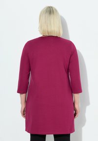 Fuksia tunika pehmeast materjalist, millel on kolmveerandiku varrukad ja sirge lõik, ulatudes just üle puusade, ilma nähtavate mustriteta.