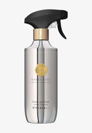 Przezroczysta butelka spray z czarnym spustem, złotymi akcentami i etykietą z napisem "Aromat Domowy Biała Bazylia" w czarnym kroju pisma.