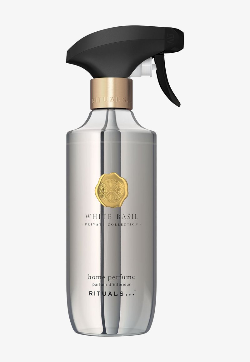 Gennemsigtig sprayflaske med en sort trigger, guld detaljer og en etikette med teksten "Hvid Basilikum Hjemmeparfume" i sort skrift.