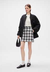 Μαύρο bomber jacket πάνω από ένα λευκό τοπ, συνδυασμένο με μια καρό μίνι φούστα σε μαύρο και άσπρο. Τα αξεσουάρ περιλαμβάνουν μια μαύρη τσάντα και μαύρες επίπεδες παπούτσια.