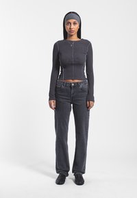 Top nero a maniche lunghe con coste, cuciture blu, abbinato a jeans scuri a vestibilità ampia e scarpe nere. Design semplice, con accenti minimi.