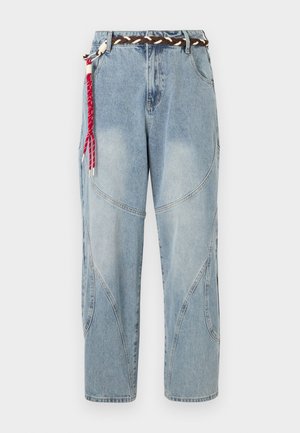 Φωτεινό μπλε τζιν με καμπυλωτές ραφές στα πάνελ και πλεκτή καφέ ζώνη με κόκκινη και λευκή υφαντή φούντα στην αριστερή πλευρά.