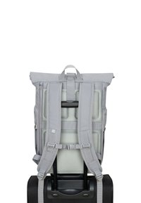 Gray roll-top backpack with adjustable padded straps and mesh back, securely attached to a black wheeled suitcase.