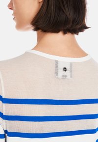 Leichtes, durchsichtiges Strickoberteil mit blauen und beigen horizontalen Streifen. Verfügt über einen weißen Kragen und ein dekoratives Etikett mit einem kreisförmigen Akzent.