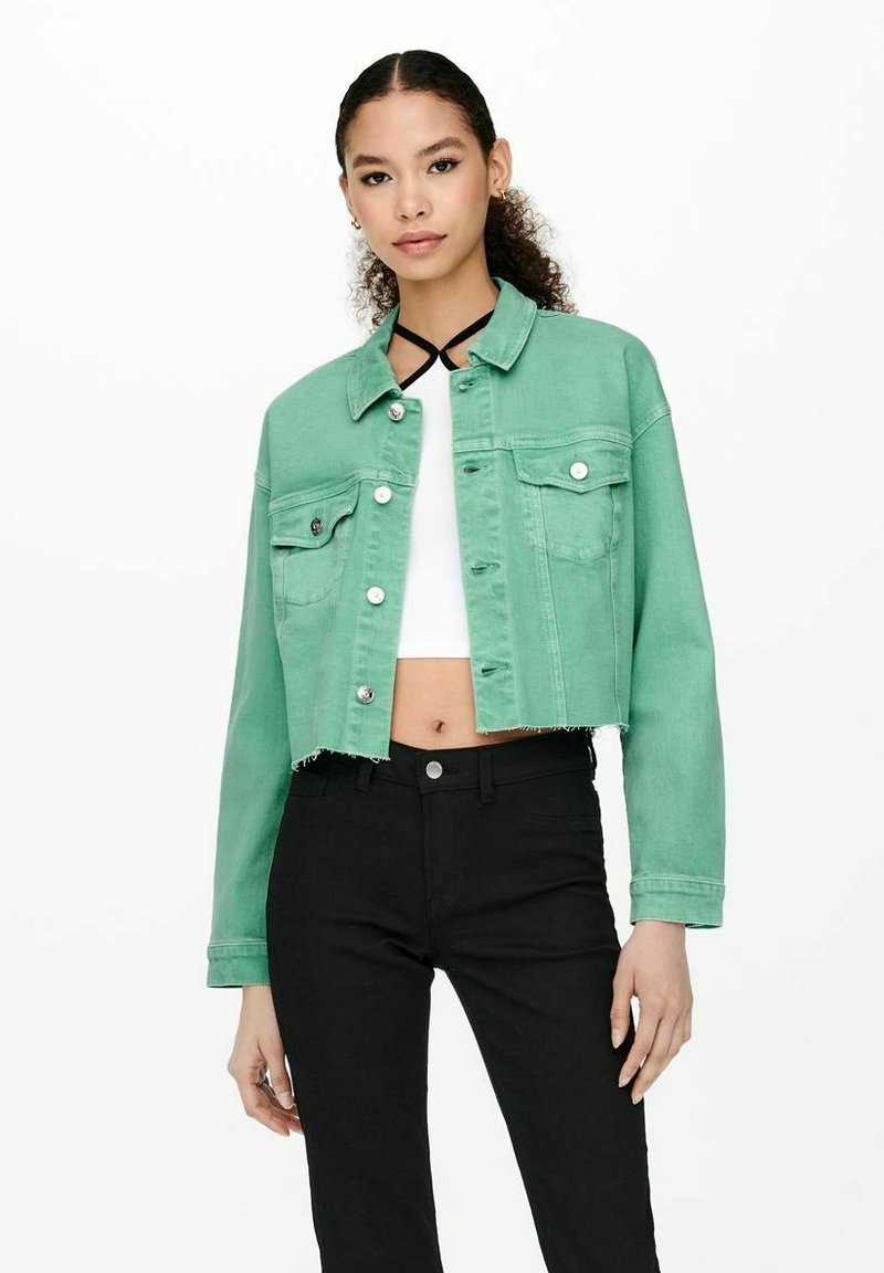 Giacca di jeans cropped verde menta con chiusura a bottoni e due tasche frontali, abbinata a una maglietta bianca e pantaloni neri a vita alta.