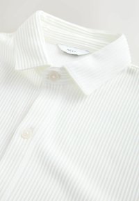 Weißes, geripptes Polohemd mit einem Kragen, ausgestattet mit einer Blende mit zwei hellen Knöpfen und einem "NEXT"-Etikett an der Rückseite des Kragens.